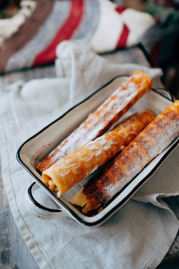 From above of crispy waffle rolls with sweet filling and powdered sugar in enameled baking dish placed on rustic wooden table